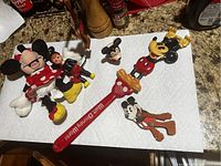 Collection of Mickey Mouse antique collectibles on a kitchen counter including wooden puppet, plastic figures, and souvenir spoon.