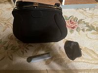 Black antique purse with gold-tone metal frame and strap, sitting closed on floral carpet with small accessory and perfume bottle next to it.
