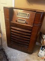 Front view of large antique wooden console radio showing wood cabinet, tuning dial, push-button controls, and speaker grille.
