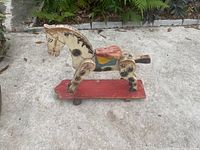 Antique wooden horse scooter showing horse figure mounted on red wooden base with metal wheels, one wheel missing