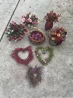 Overview of all nine artificial floral arrangements and heart-shaped wreaths set on concrete ground