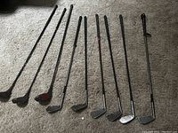 Photo of nine antique golf clubs with steel shafts, some designed with a wood look.