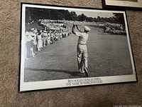 Framed black and white photo showing Ben Hogan mid golf swing with spectators in background, mounted on wall.