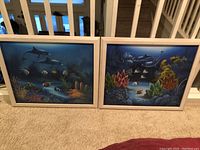 Two framed canvas paintings side by side showing underwater ocean scenes with dolphins, coral reefs, and tropical fish.