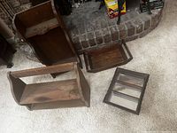 Photo showing two small wooden wall cabinets and a small shelf unit with mirrors on a carpeted floor near a brick fireplace.