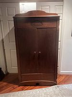 Front view of closed antique Early American armoire with carved drawer front and double doors.