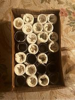 Top view of a box containing mostly white tissue-paper wrapped Edison phonograph cylinders, with some black unwrapped cylinders visible.