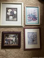Four framed matted prints and one canvas with purple frame laid out on carpet. Floral, fruit still life, and garden scenes with a lady.