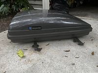 Closed view of the dark grey hard shell GM luggage carrier with GM Accessories badge, showing exterior surface and mounting clamps underneath.