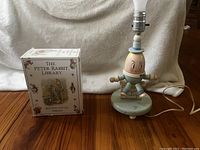 Photo showing Humpty Dumpty lamp next to Peter Rabbit Library box of ten books on wooden floor with white textured background.