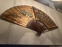 Photo of the full fan spread open mounted on the wall showing the floral and mountain artwork on paper or fabric.