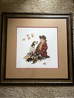 Full view of one framed Norman Rockwell print showing a boy in a red plaid jacket sitting with puppies and autumn leaves.