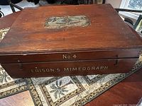 Closed wooden case of Edison Mimeograph No. 4 showing 'EDISON'S MIMEOGRAPH' on front and aged wood surface.
