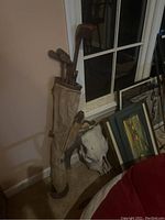 Set of antique hickory shaft golf clubs standing inside original antique golf bag, placed by a wall near a window.