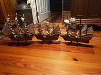 Three wooden ship models displayed side by side on a wooden floor showcasing overall size and scale.