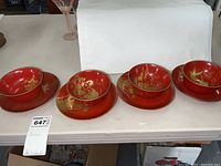 Four Japanese lacquerware sets each with a red bowl and matching red plate, all decorated with gold designs depicting fish, foliage, and flora.
