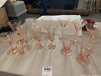 Full set of 13 pink Depression glass glasses arranged on table showcasing variety of styles including tall flared glasses, stemmed goblets, and smaller glasses.