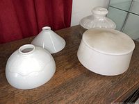 Four vintage white glass lampshades of different shapes on wooden surface with red curtain background, showing general lot condition and size