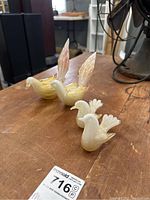 Four Murano glass bird paperweights arranged on a wooden surface, showing two larger yellow-cream birds with flame-like tails and two smaller white-orange birds with fanned tails.