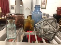 Three glass bottles and a glass cube displayed together on a rack.