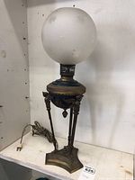 Full view of the antique lamp showing the frosted glass globe atop the ornate brass and bronze body with electric cord.