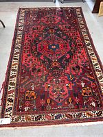 Full view of the red hand woven Afghan wool rug showing entire pattern, color detail, and condition including edge wear.