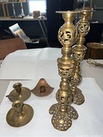 Two tall vintage brass candlestick holders with openwork detail and three smaller brass candle holders arranged together