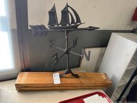Front view of vintage cast metal clipper ship weathervane on wooden block, showing directional letters and arrow.