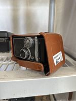 Side view of the vintage black Yashica camera inside a tan leather case showing manual dials and textured finish