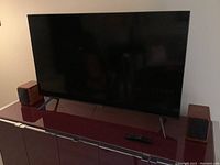 Front view of TV on cabinet with remote and speakers