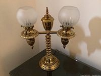 Full view of brass table lamp with two frosted glass globe shades on black surface.