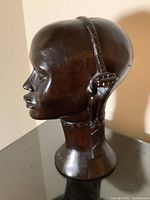Carved wooden bust shown from side angle, highlighting the profile and detailed carving of facial features and ornamental headband.