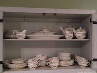 Photo of dinnerware set arranged on two shelves showing plates, bowls, teapots, and cups in Cowslip pattern with floral design.