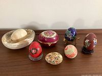 Whole set of decorative eggs, Limoges trinket box in burgundy with gold accents, large stone bowl with matching stone egg, displayed on wooden surface