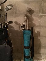 Two golf bags filled with clubs leaning against cinderblock wall
