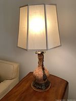 Lamp illuminated showing hexagonal light cream shade atop mottled reddish stone base with ornate dark metal accents and round base plate