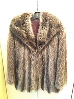 Full view of the natural raccoon fur coat hanging on a hanger, showing the fur pattern and overall shape.