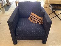 Front view of a dark blue club chair with small grey and tan dots and a decorative throw pillow