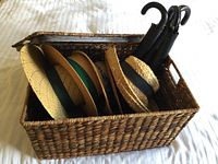 Woven basket holding three black umbrellas and five straw hats arranged vertically.