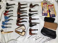 Overview of tobacco pipes, cases, cleaner packets and tools laid out on white cloth