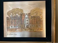 Close-up photo showing 'The Michigan League' etching on metal with detailed building and tree imagery in autumn colors, mounted on dark matte and framed in gold.