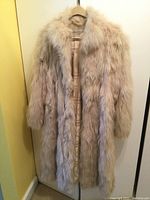 Front view of full-length cream-colored fox belly fur coat hanging on hanger.