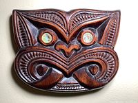 Close-up photo of larger carved wooden face showing moko details and pearlescent abalone eyes