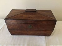 Front view of rectangular wooden box with hinged lid closed. Shows keyhole escutcheon on front.