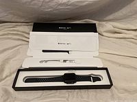 Packaging open showing watch, extra band piece, magnetic charging cable, and documentation
