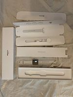 Apple Watch Series 3 with white sport band, magnetic charging cable, and box inserts laid out.