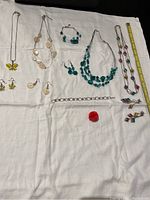 Full view of all 11 assorted vintage costume jewelry pieces arranged on white fabric, showing necklaces, bracelets, earrings, and a pin.