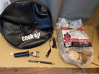 Cook-Air branded black carrying case, small USB charger cable, small fan unit, and metal scraping tool on beige surface.