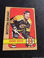 Photo of front side of Johnny Bucyk hockey card from 1972-73 season showing player portrait and team name Boston Bruins.