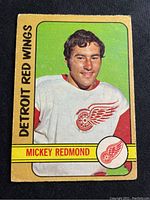 Front side of 1972-73 O-Pee-Chee Mickey Redmond hockey card showing image of player in Detroit Red Wings jersey with yellow and green borders and visible crease on front bottom left.